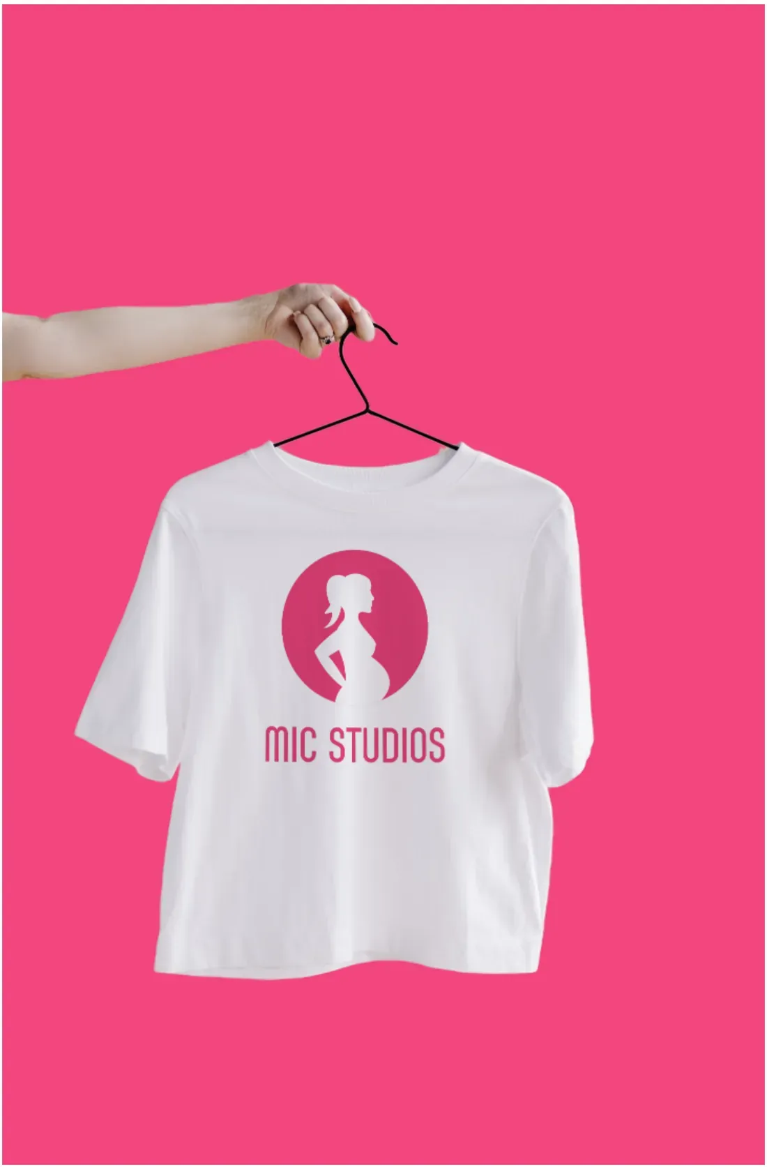 White t-shirt on a hanger with the MIC Studios logo, against pink