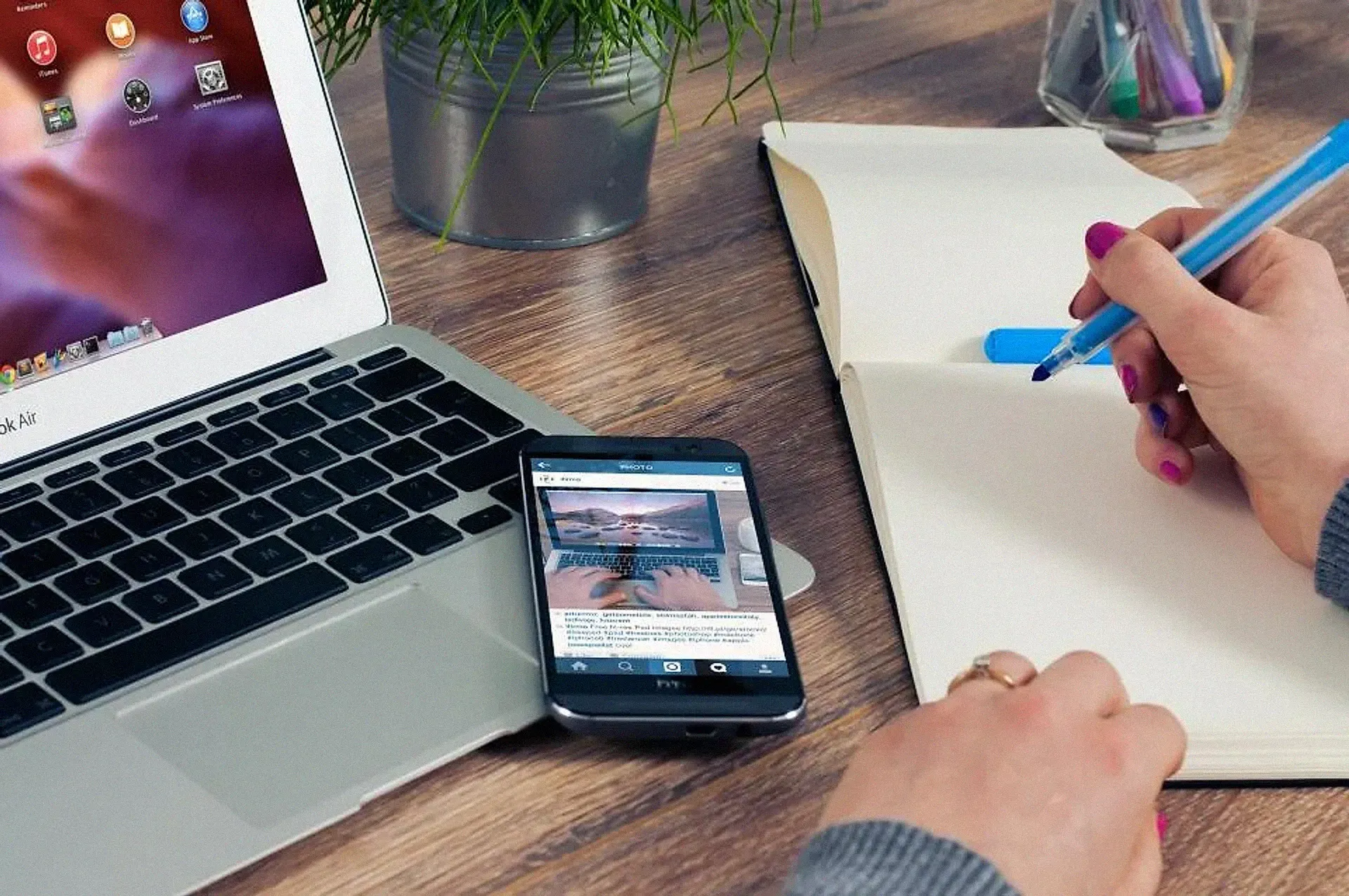 A laptop and phone beside a notebook with a hand writing