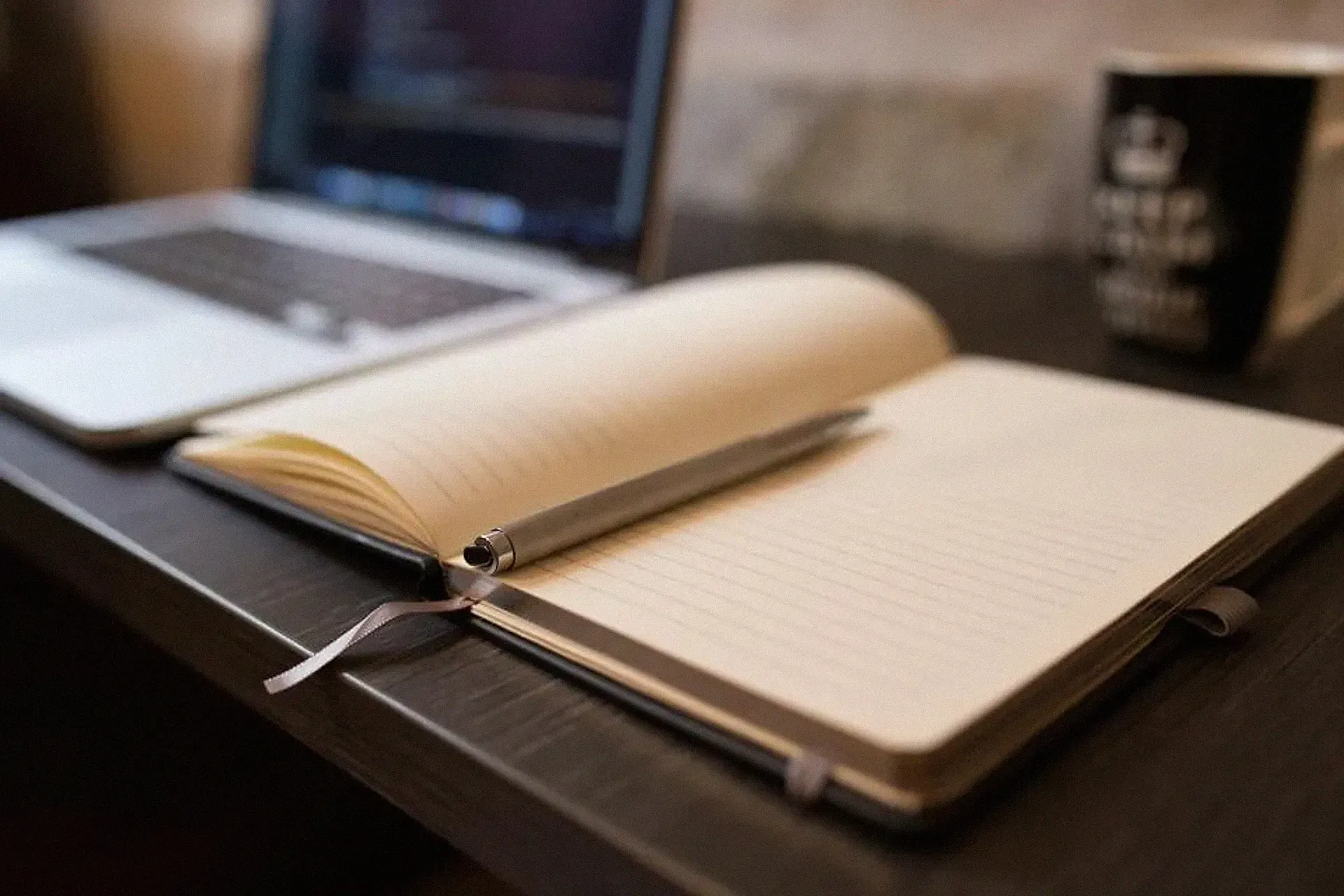 A notebook open on a desk beside a laptop