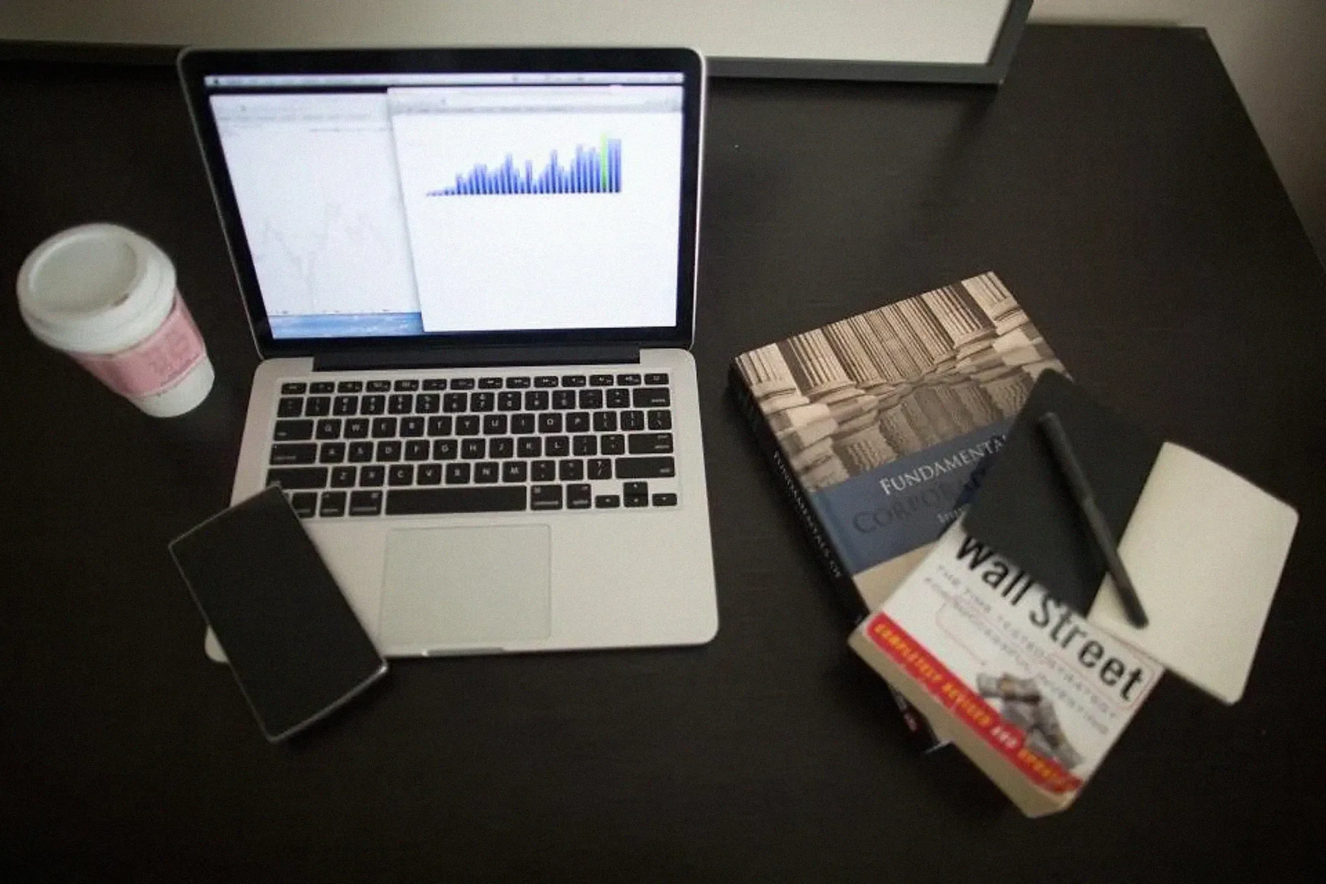 A laptop showing a performance chart on a dark desk with a phone and book