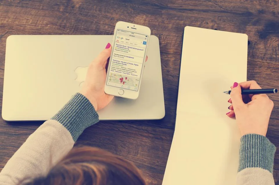 A hand holding a phone beside an open notebook and pen