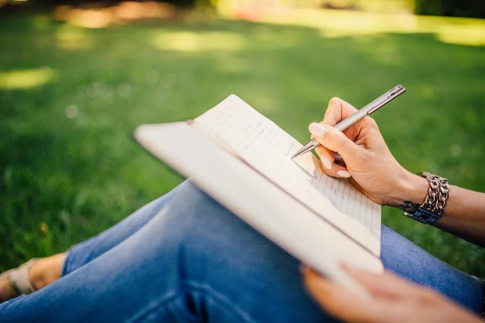 A person writing in a notebook on the grass