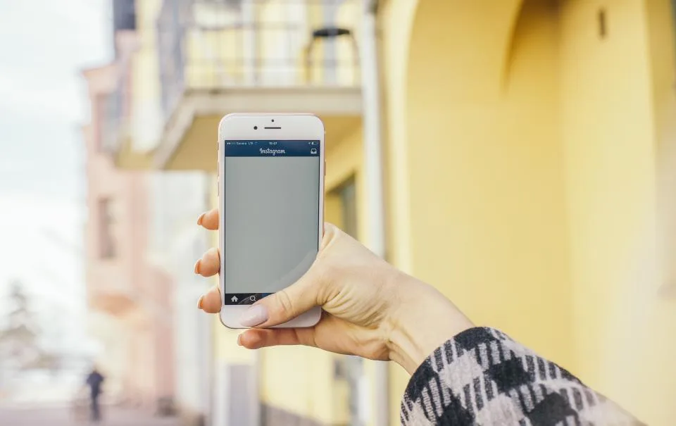 A hand holding up a smartphone in a sunlit street